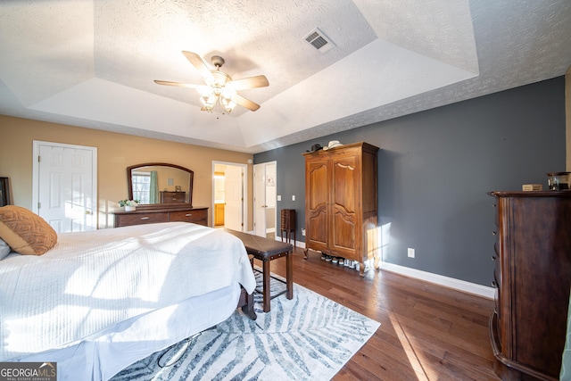 bedroom featuring ceiling fan, dark wood-type flooring, a textured ceiling, and a tray ceiling