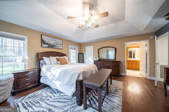 bedroom featuring ceiling fan, connected bathroom, a raised ceiling, and multiple windows