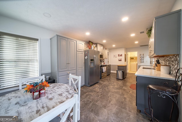 kitchen with appliances with stainless steel finishes, gray cabinetry, tasteful backsplash, washer / clothes dryer, and sink