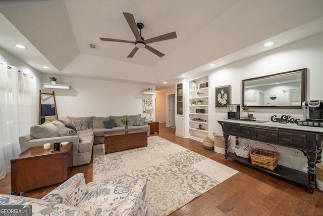 living room featuring ceiling fan, dark hardwood / wood-style flooring, a tray ceiling, and built in shelves