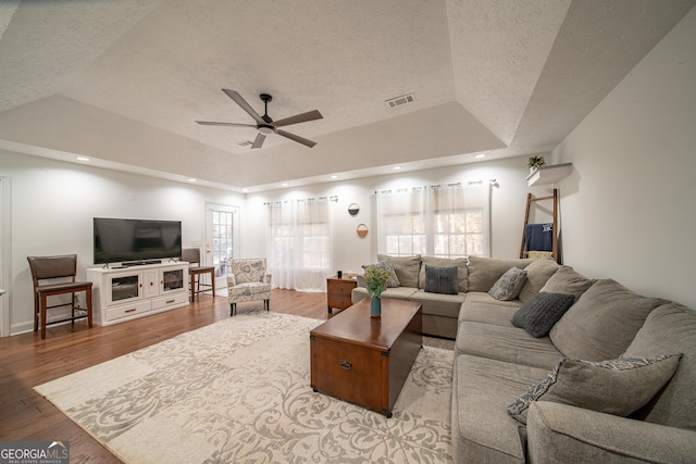 living room with a raised ceiling, ceiling fan, a textured ceiling, and light hardwood / wood-style floors