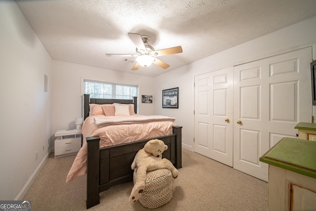 bedroom featuring ceiling fan, light colored carpet, a textured ceiling, and a closet