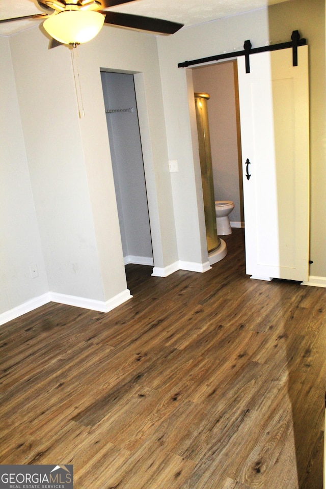 unfurnished bedroom with ensuite bath, dark hardwood / wood-style floors, a closet, ceiling fan, and a barn door