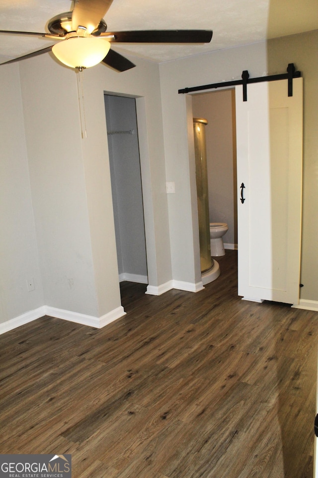 unfurnished bedroom with a barn door, ceiling fan, dark hardwood / wood-style floors, ensuite bath, and a closet