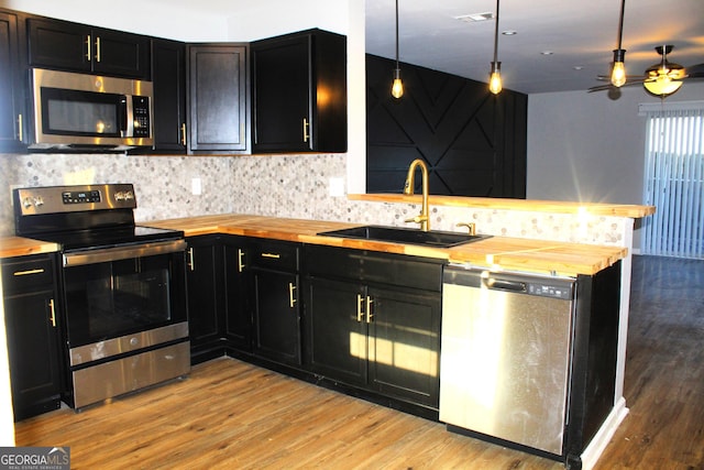 kitchen with butcher block counters, kitchen peninsula, stainless steel appliances, pendant lighting, and sink