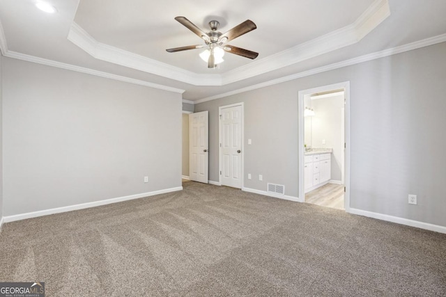 unfurnished bedroom featuring ceiling fan, light colored carpet, a tray ceiling, and ensuite bath