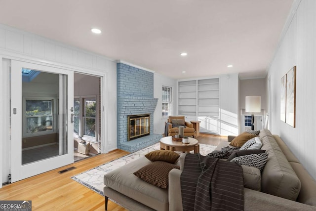 living room featuring a brick fireplace, ornamental molding, hardwood / wood-style flooring, and built in shelves