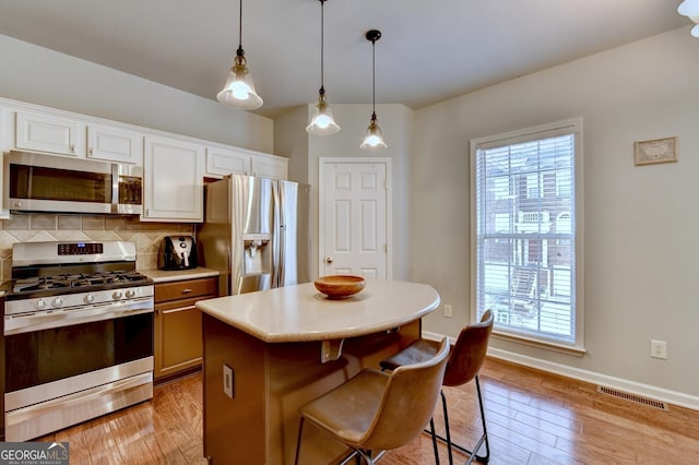 kitchen featuring pendant lighting, white cabinets, appliances with stainless steel finishes, decorative backsplash, and a breakfast bar