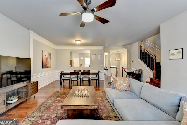 living room featuring wood-type flooring, ceiling fan with notable chandelier, and ornamental molding