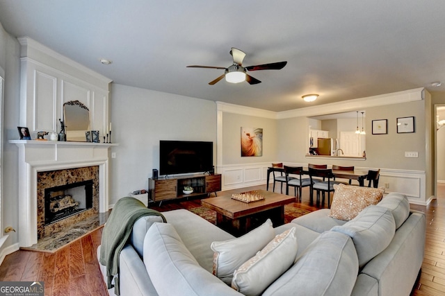 living room featuring ceiling fan, a high end fireplace, crown molding, and wood-type flooring