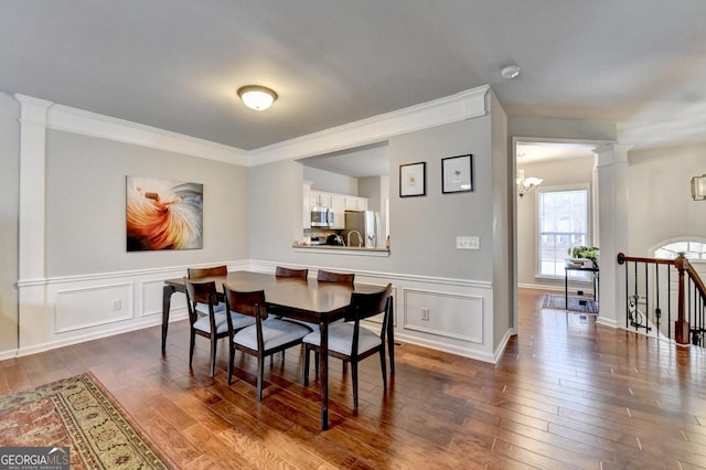 dining room featuring dark hardwood / wood-style floors, decorative columns, ornamental molding, and a notable chandelier