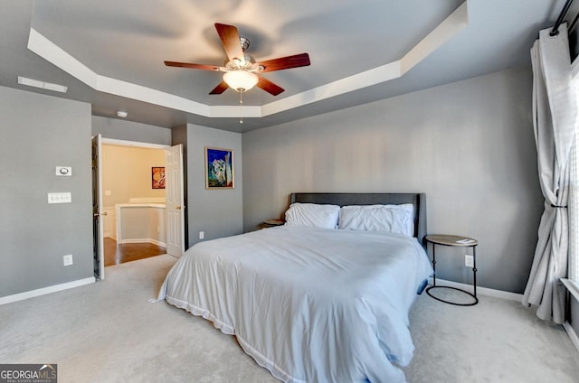 bedroom featuring a raised ceiling, light colored carpet, and ceiling fan