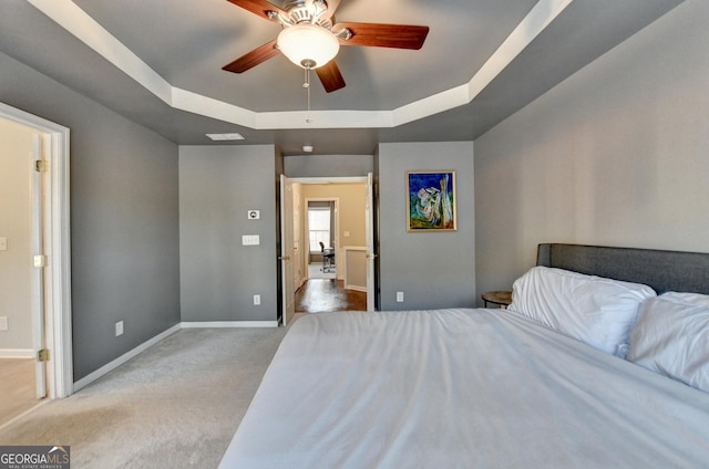 carpeted bedroom with ceiling fan and a tray ceiling