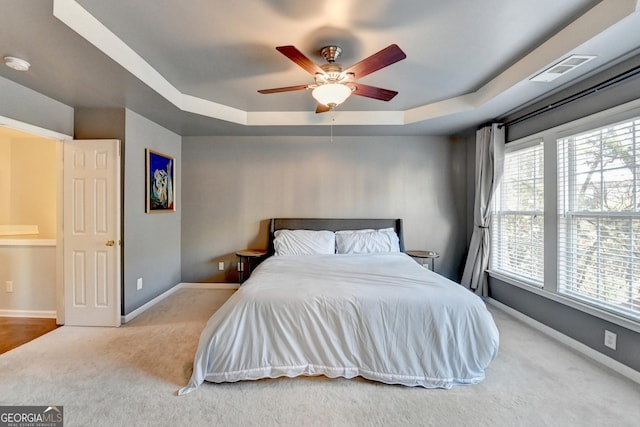 carpeted bedroom with ceiling fan and a tray ceiling