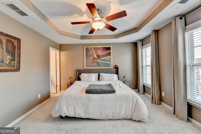 carpeted bedroom with a raised ceiling and ceiling fan