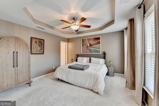 bedroom featuring ceiling fan, light colored carpet, and a tray ceiling