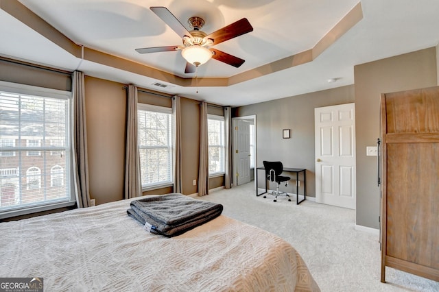 carpeted bedroom featuring ceiling fan, a tray ceiling, and multiple windows