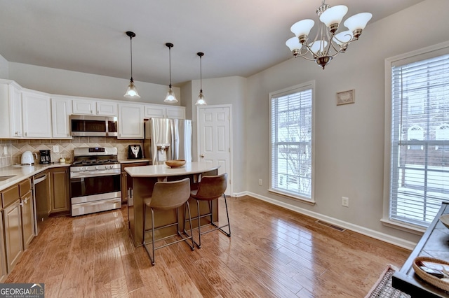 kitchen featuring decorative light fixtures, backsplash, a notable chandelier, a kitchen island, and appliances with stainless steel finishes