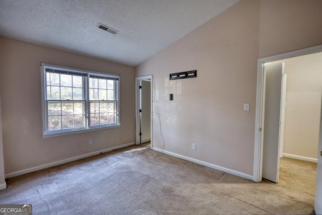 spare room with lofted ceiling, light colored carpet, and a textured ceiling