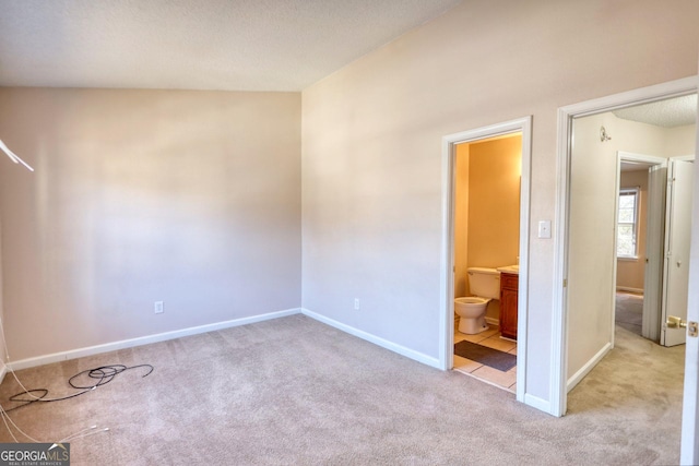 unfurnished bedroom featuring ensuite bathroom and light colored carpet