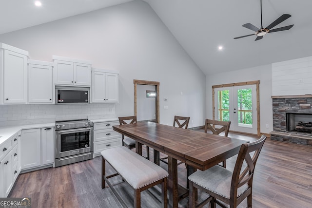 dining space featuring dark wood-type flooring, ceiling fan, a stone fireplace, and high vaulted ceiling