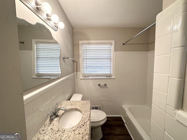 full bathroom with wood-type flooring, sink, tile walls, toilet, and  shower combination