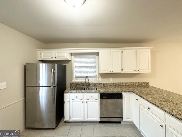 kitchen featuring white cabinetry, stainless steel appliances, light tile patterned flooring, dark stone counters, and sink