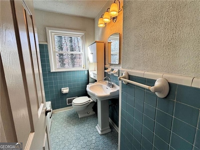 bathroom featuring toilet, tile walls, a textured ceiling, and tile patterned flooring