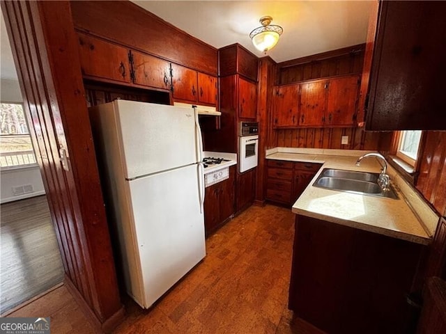 kitchen with wooden walls, dark wood-type flooring, sink, and white appliances