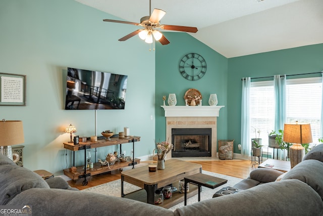 living room featuring vaulted ceiling, ceiling fan, a tiled fireplace, and hardwood / wood-style floors