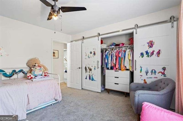 bedroom featuring ceiling fan, a barn door, a closet, and light colored carpet