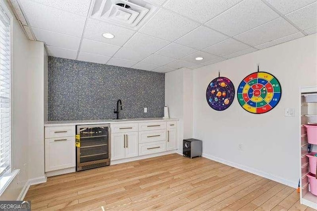 bar with light hardwood / wood-style floors, decorative backsplash, sink, white cabinets, and beverage cooler