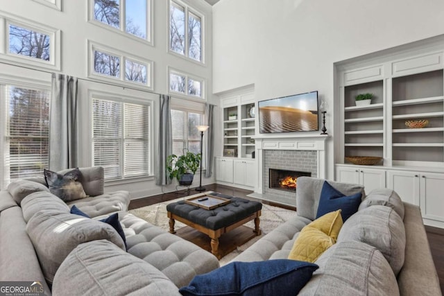 living room with hardwood / wood-style floors, plenty of natural light, a fireplace, built in features, and a towering ceiling