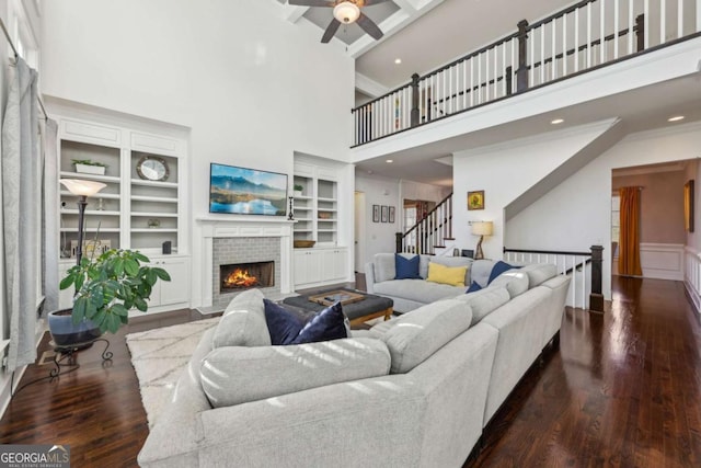 living room featuring a fireplace, built in features, a towering ceiling, and ornamental molding