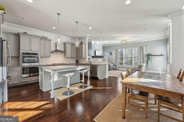 kitchen with appliances with stainless steel finishes, a center island, wall chimney exhaust hood, gray cabinetry, and crown molding