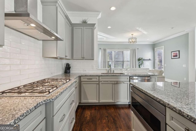 kitchen featuring appliances with stainless steel finishes, tasteful backsplash, wall chimney range hood, light stone counters, and sink