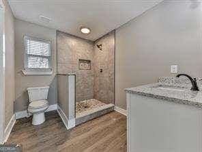 bathroom with wood-type flooring, toilet, vanity, and a tile shower