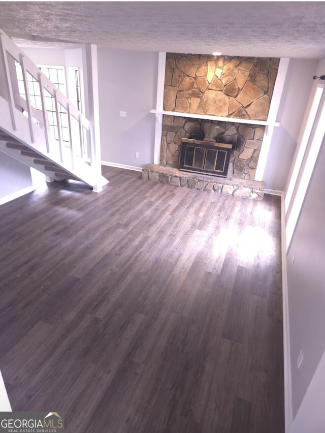 unfurnished living room with dark wood-type flooring and a stone fireplace