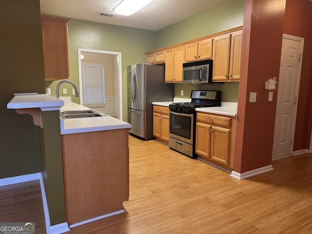 kitchen featuring stainless steel appliances, sink, a textured ceiling, and light hardwood / wood-style floors