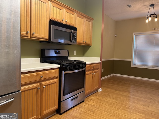 kitchen featuring stainless steel appliances, hanging light fixtures, a textured ceiling, and light wood-type flooring