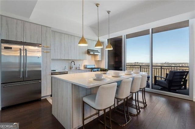 kitchen featuring dark hardwood / wood-style floors, stainless steel built in fridge, decorative light fixtures, a center island, and sink