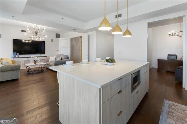 kitchen with stainless steel microwave, a raised ceiling, a chandelier, and a kitchen island