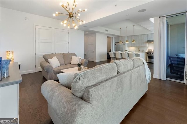 living room featuring a raised ceiling, dark hardwood / wood-style flooring, and an inviting chandelier