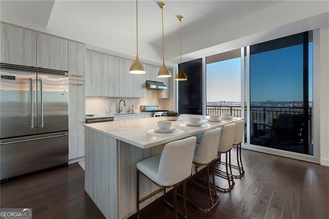 kitchen featuring built in fridge, a kitchen island, decorative light fixtures, dark wood-type flooring, and sink