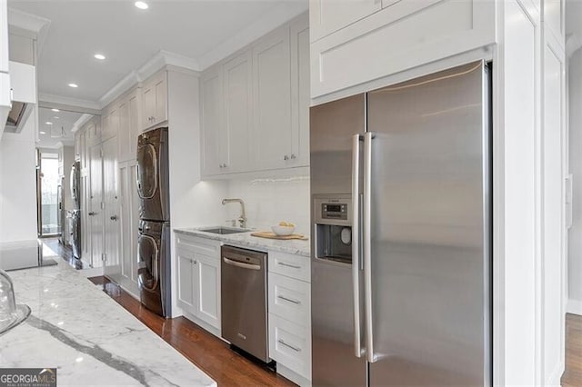 kitchen featuring stacked washer / drying machine, sink, white cabinetry, appliances with stainless steel finishes, and light stone countertops