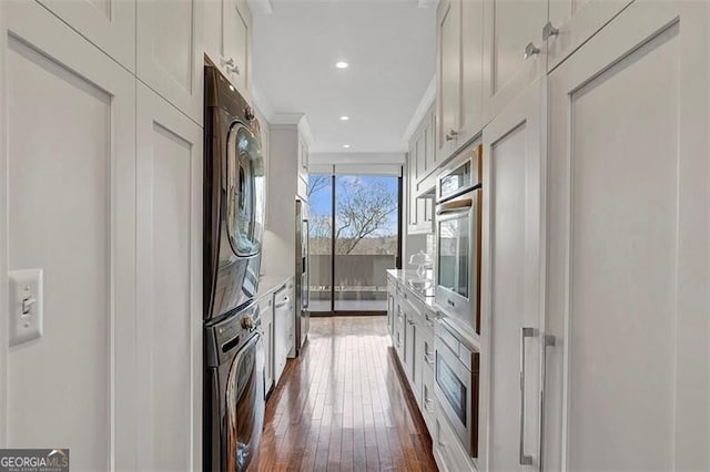 kitchen with stacked washing maching and dryer, dark hardwood / wood-style floors, white cabinets, stainless steel oven, and wall oven