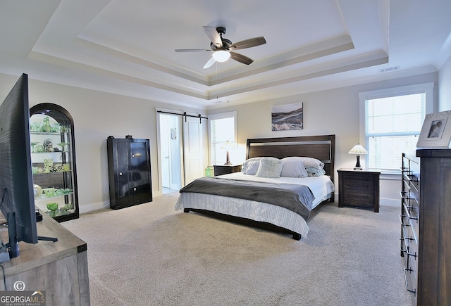 carpeted bedroom featuring a raised ceiling, ornamental molding, a barn door, and ceiling fan