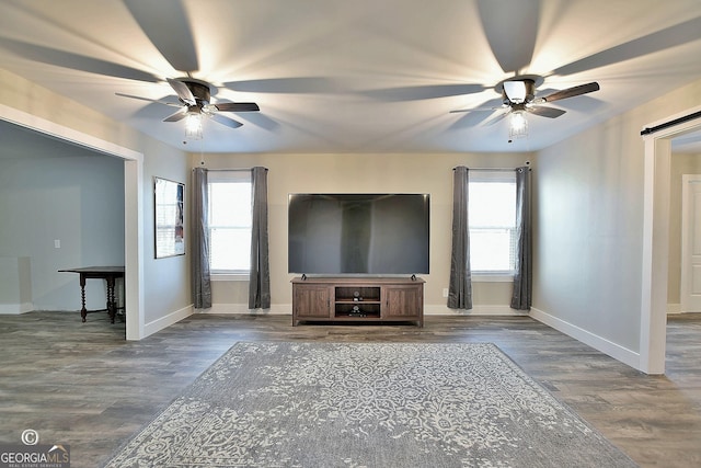 unfurnished living room with dark hardwood / wood-style flooring, plenty of natural light, a barn door, and ceiling fan