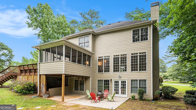 rear view of house with a sunroom, a deck, french doors, a patio, and a lawn