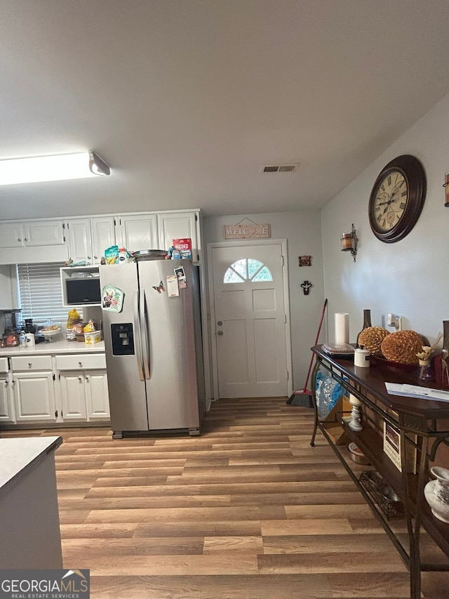 kitchen with stainless steel fridge with ice dispenser, white cabinetry, and light wood-type flooring